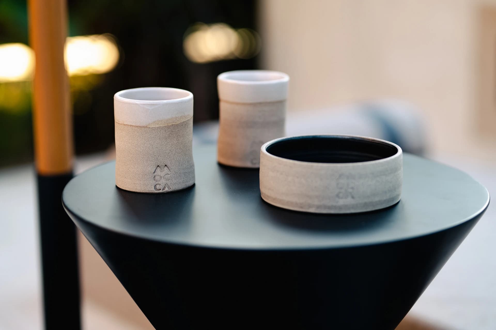 Handmade ceramic cups and a bowl on a dark round table